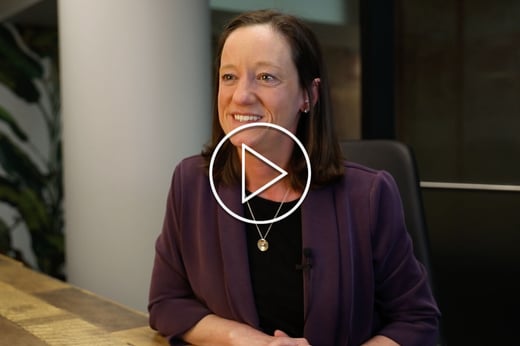 A protrait of Wil Del Pilar, Ph.D. wearing a dark blazer and black and white dress shirt. There is a white stenciled play button in the fore front.