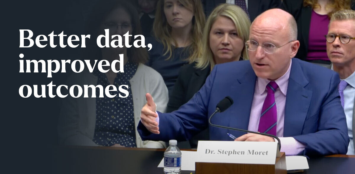 In white, text says better data, improved outcomes. Stephen Moret is sitting down testifying in front of a committee. There is a crowd behind him.