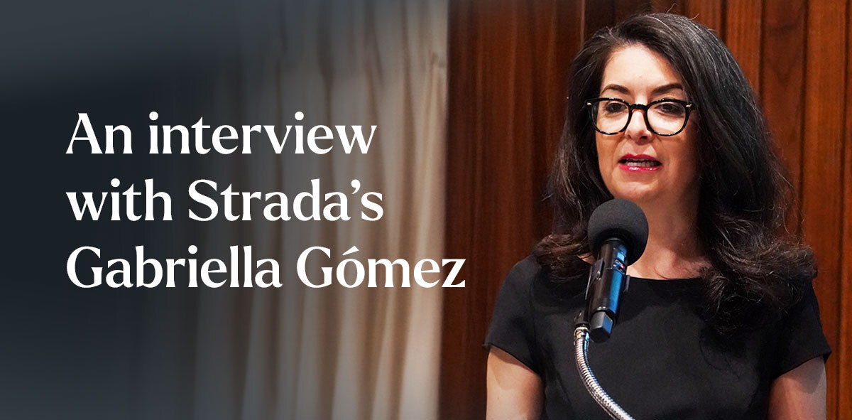 In white, text says An interview with Strada's Gabriella Gómez. There is a candid photo of Gabriella to the right speaking from a microphone. 